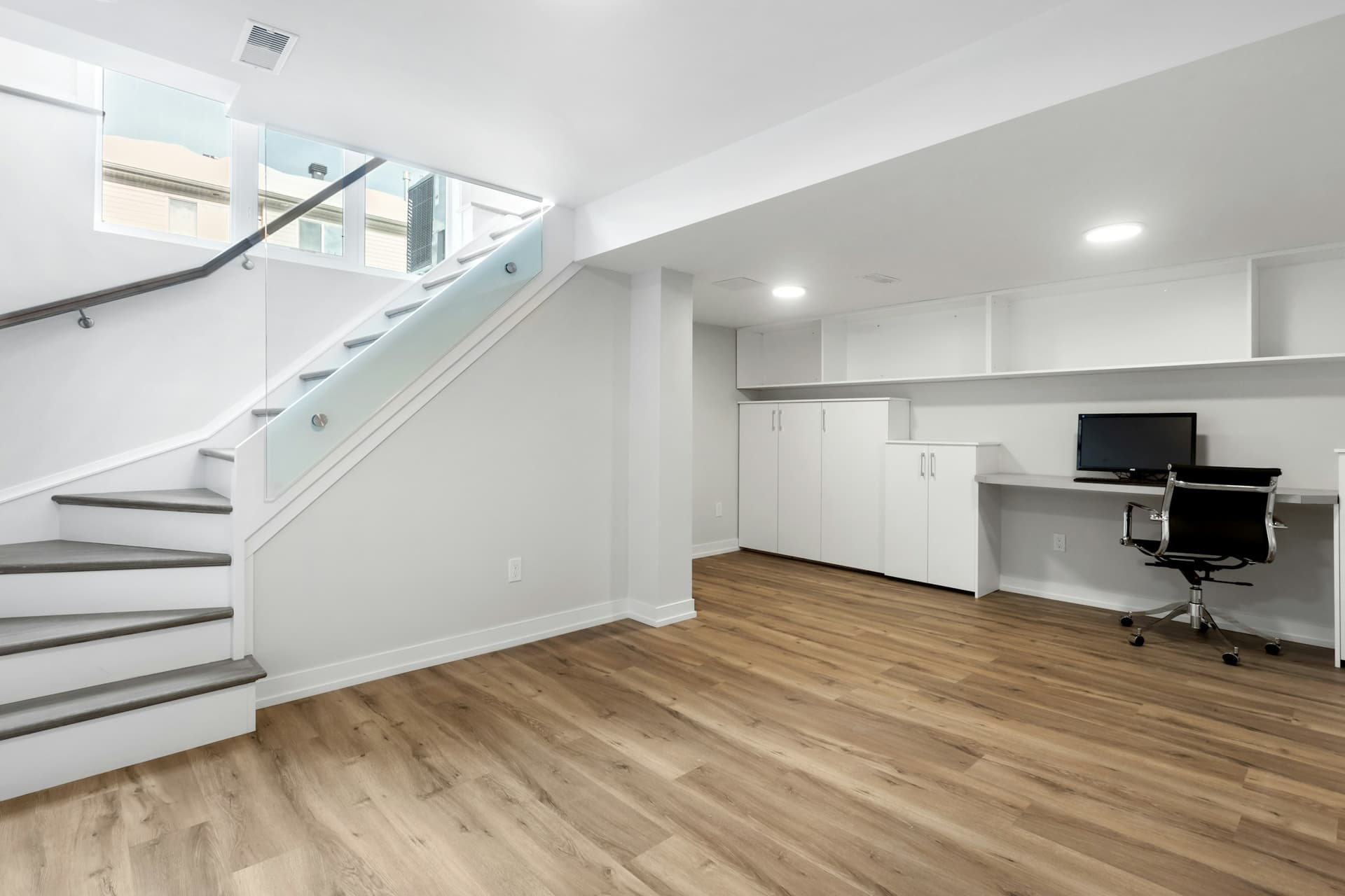 Finished basement home office with wood-look flooring and a modern staircase